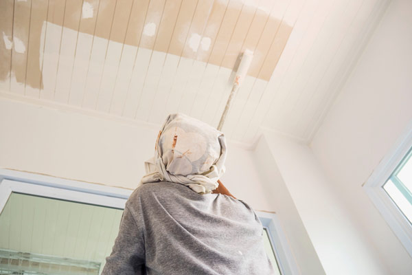 A person painting a ceiling with a paint brush, adding color and life to the surface above.