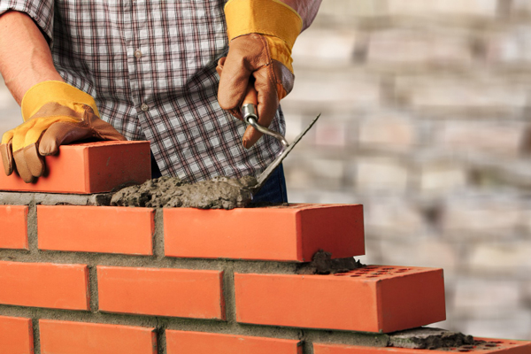 A man constructing a brick wall with precision and focus, carefully placing each brick in its designated spot.